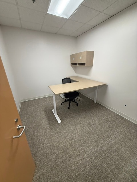 Private office with L-desk, overhead storage, and task chair